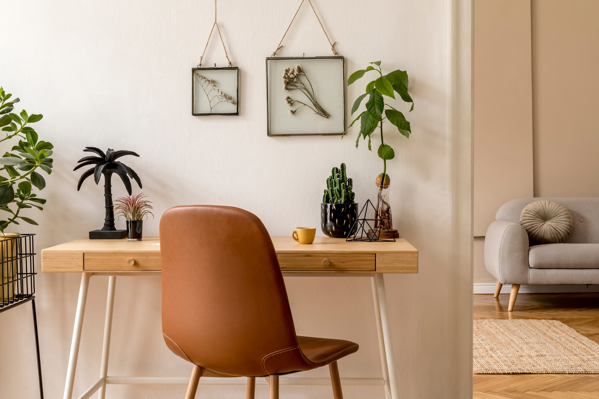 Interior design of scandinavian open space with mock up photo frames, wooden desk, gray sofa, cacti, books office and personal accessories. Stylish neutral home staging. Beige walls. Template.